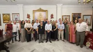Grupo de personas posando en sala con cuadros religiosos y suelo de mármol durante presentación de la nueva Junta de Gobierno de la Hermandad de Olivares