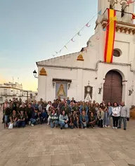 Grupo numeroso de peregrinos posando frente a una iglesia blanca decorada con banderas y guirnaldas en un ambiente festivo y devocional