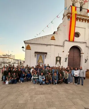 Grupo numeroso de peregrinos posando frente a una iglesia blanca decorada con banderas y guirnaldas en un ambiente festivo y devocional