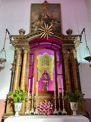 Altar barroco con columnas doradas y fondo de damasco fucsia, decorado con ramos de rosas, candeleros de plata y pintura religiosa sobre la Virgen pastora